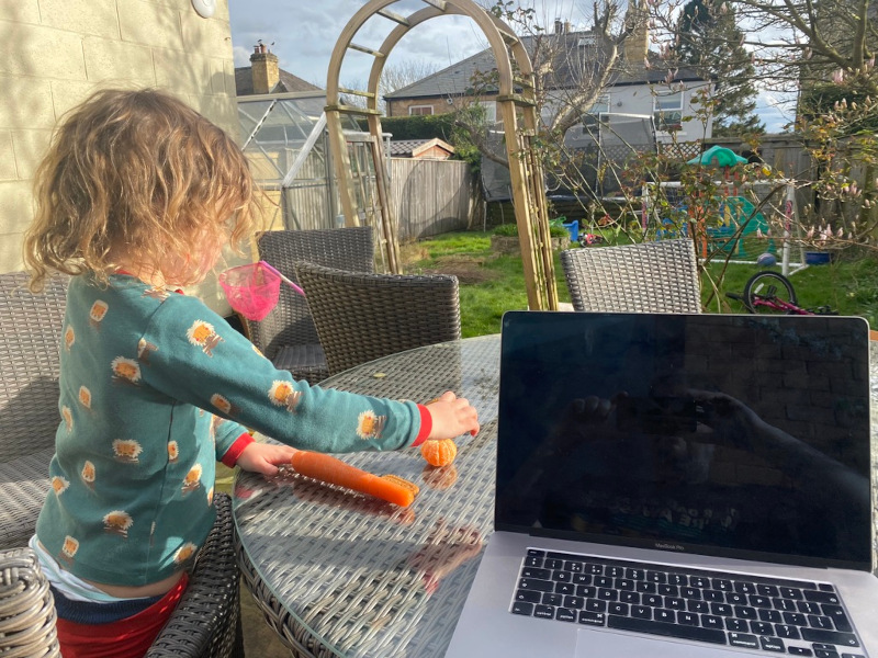 Computer on garden table next to young child