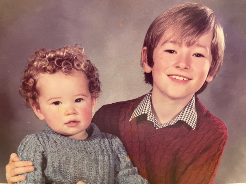 Portrait photo of smiling older brother holding young child taken in 1980s